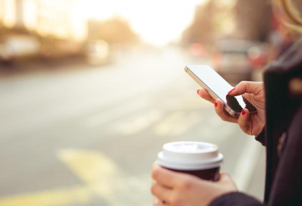 Imagen de una mujer usando un móvil y con un café en la otra mano