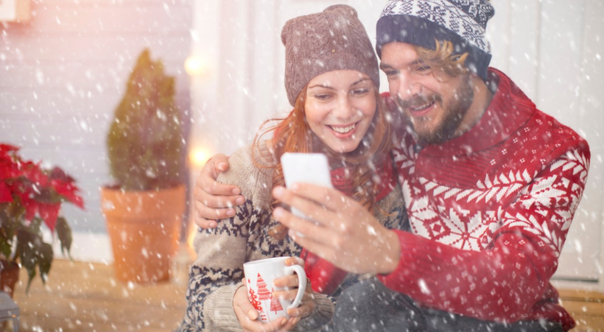 Imagen de un chico y una chica en un paisaje nevado mirando el móvil
