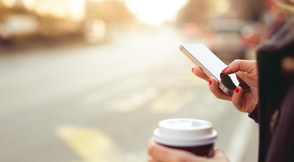 Mujer usando un móvil con un café en la oytra mano