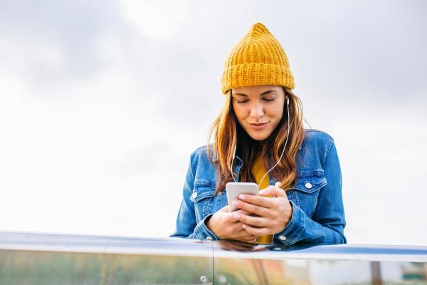 Mujer joven sonriente con gorro amarillo mirando el móvil