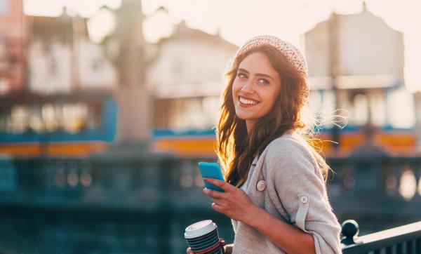 Mujer sonriendo con un móvil en una mano y café en la otra