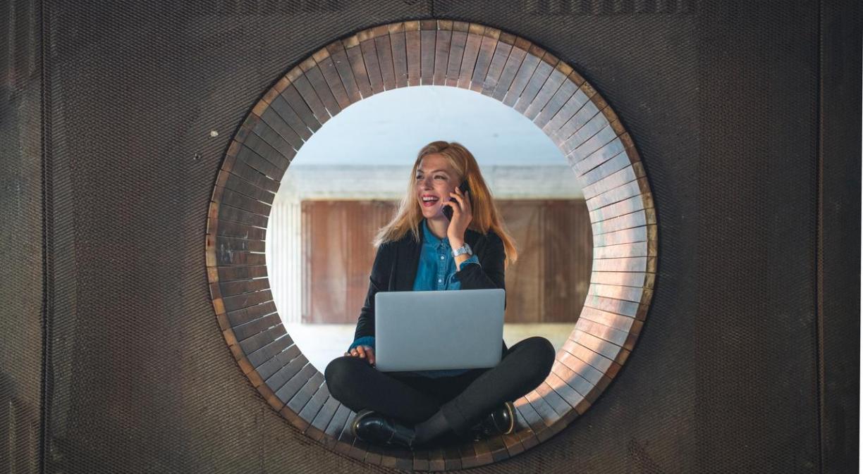 Mujer sonriente con un ordenador trabajando sentada en una ventana