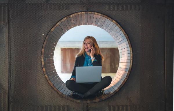 Mujer sonriente con un ordenador trabajando sentada en una ventana