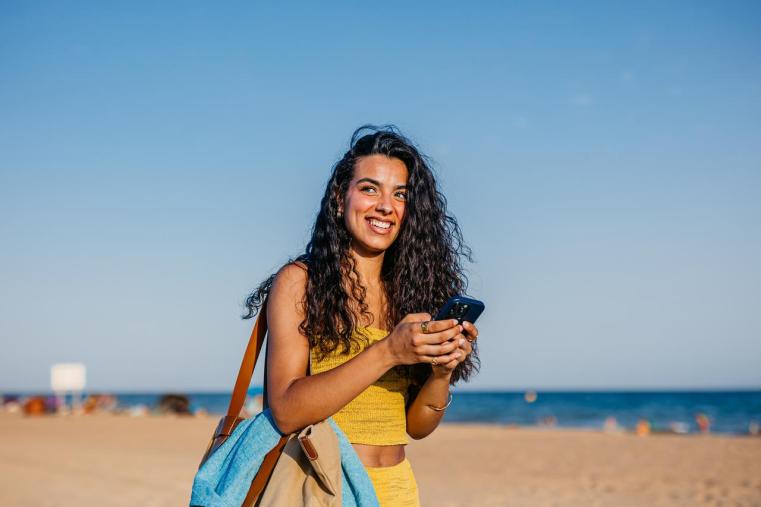 Chica joven usando móvil mientras camina por la playa
