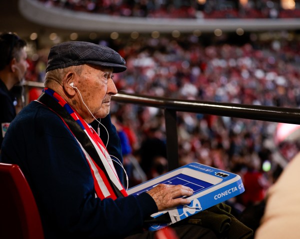 Un aficionado con bufanda del Atlético de Madrid y una tablet y cascos para seguir el partido con el audio y el tacto
