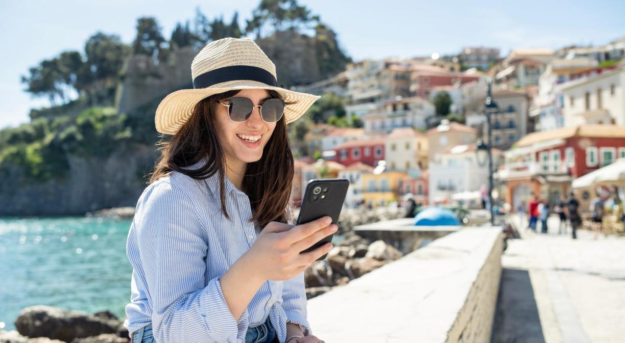 Mujer con sombrero usando su teléfono móvil en un paseo marítimo