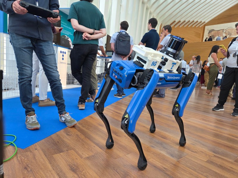 Un robot similar a un perro dirigido con un mando a distancia por una persona a la que se ve medio cuerpo