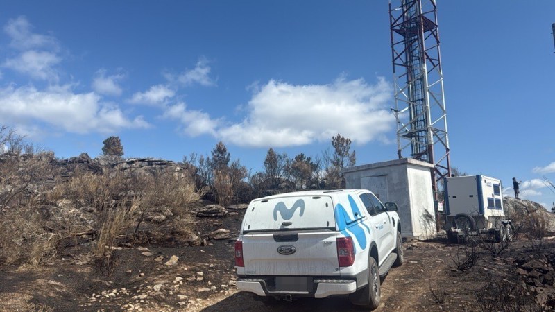 Coche de Movistar delante de una antena en un campo incendiado
